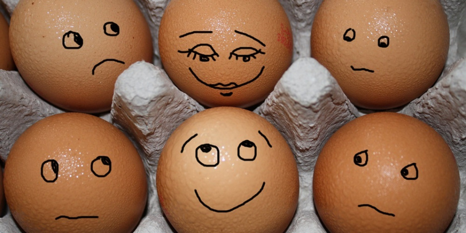 A imagem mostra quatro ovos em uma caixa de papelão. Cada ovo tem um rosto desenhado sobre a sua superfície mostrando diferentes emoções.