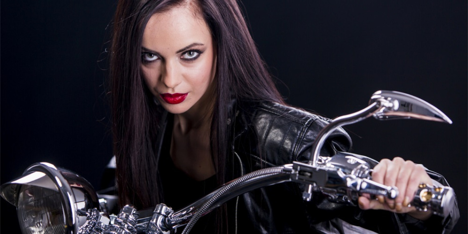 Uma mulher sedutora olha para frente de forma desafiadora. Ela está sentada em uma moto.