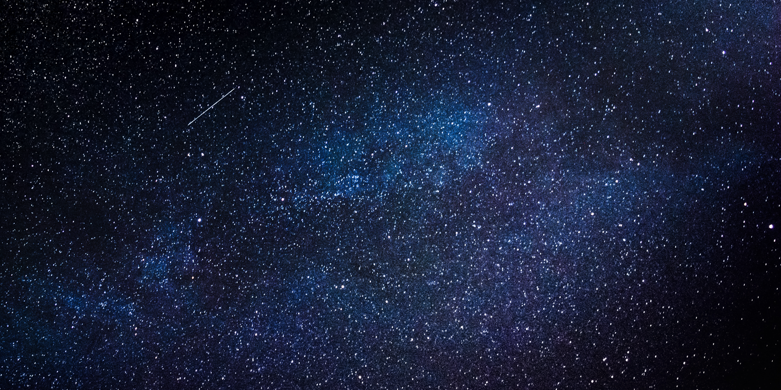 Uma noite escura e um céu cheio de estrelas. Em um ponto é possível ver uma estrela cadente.