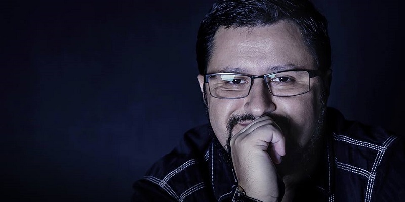 Foto do escritor Fábio M. Barreto. Ele está à frente de um fundo neutro. Só a cabeça e os ombros aparecem. Ele olha para frente, sorrindo, enquanto a mão está apoiada sobre a boca.