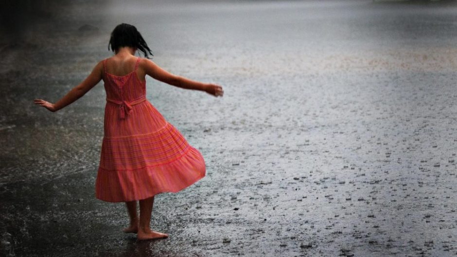 Uma garota de vestido vermelho e braços abertos sob a chuva