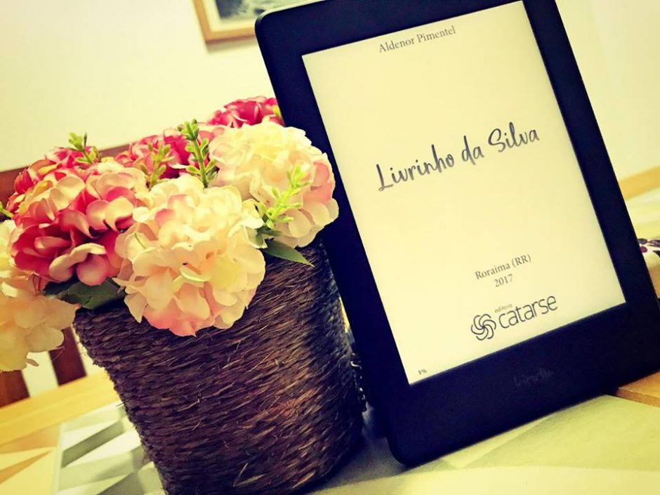 Kindle com o ebook livrinho da silva na tela e ao lado, um vaso de flores