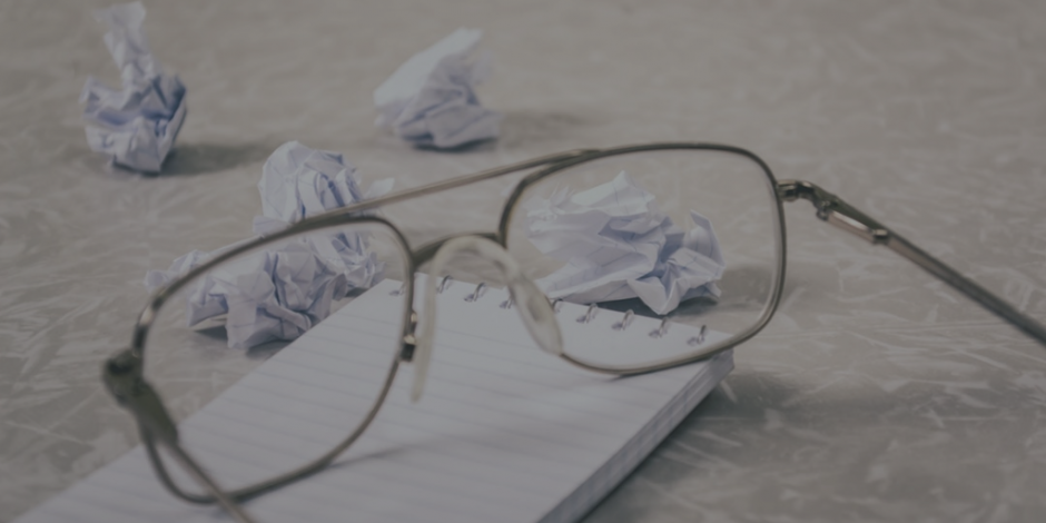 oculos sobre bloco de anotações e diversas bolas de papel sobre uma mesa